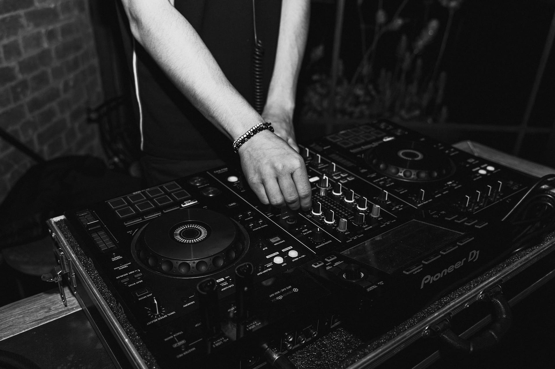 Black and white photo of a DJ using a sound mixer at a club, showcasing nightlife and music culture.